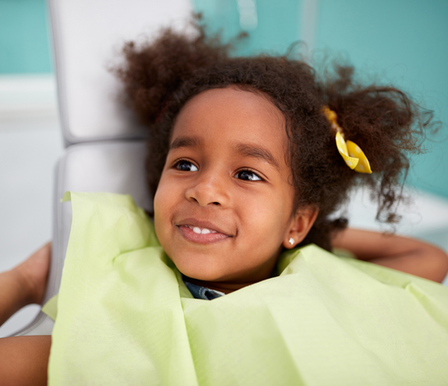 Happy young child in yellow shirt smiling at dental office with turquoise background
