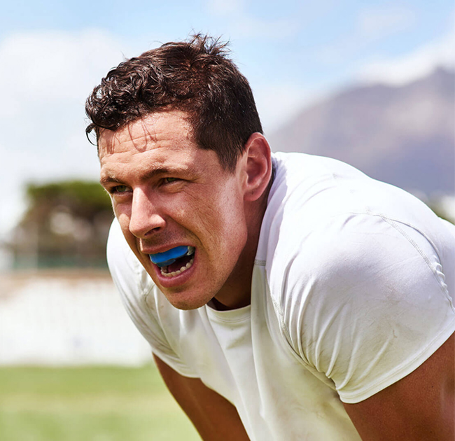 Man wearing blue mouthguard in white shirt outdoors at sports field smiling