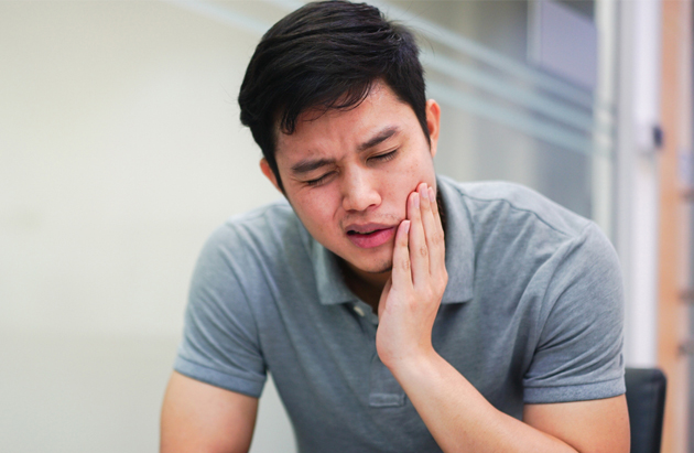 Man holding cheek in pain, dental office setting, experiencing tooth or jaw discomfort