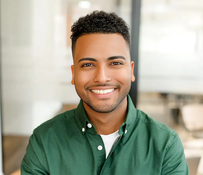 Smiling male dental professional in green shirt against blurred office background.