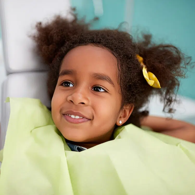 Young child smiling at camera wearing yellow shirt in dental office setting.