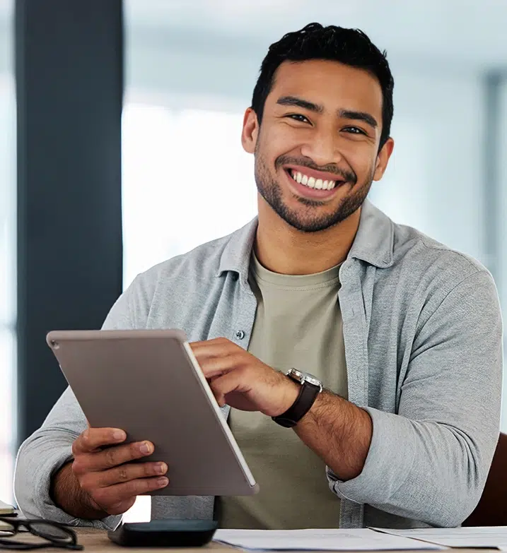 Smiling male professional holding tablet in modern office setting, wearing casual button-up shirt.