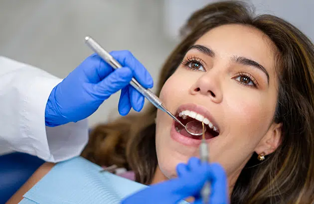 Dentist in blue gloves examining patient's teeth during dental checkup appointment.