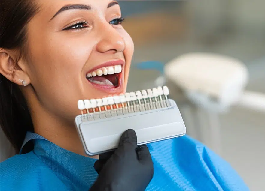 Woman smiling while holding dental shade guide for tooth color matching at dentistry office.