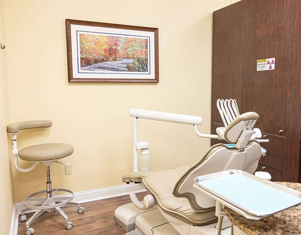 Modern dental operatory with chair, overhead light, and equipment in clean clinical setting.