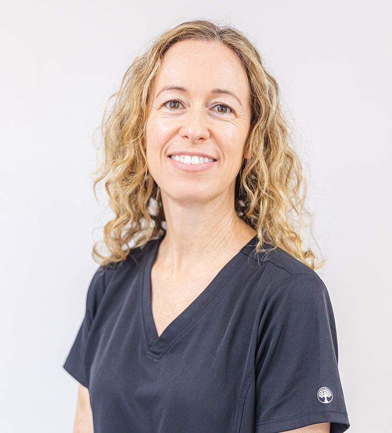 Professional headshot of a woman in dark scrubs smiling at camera against white background.