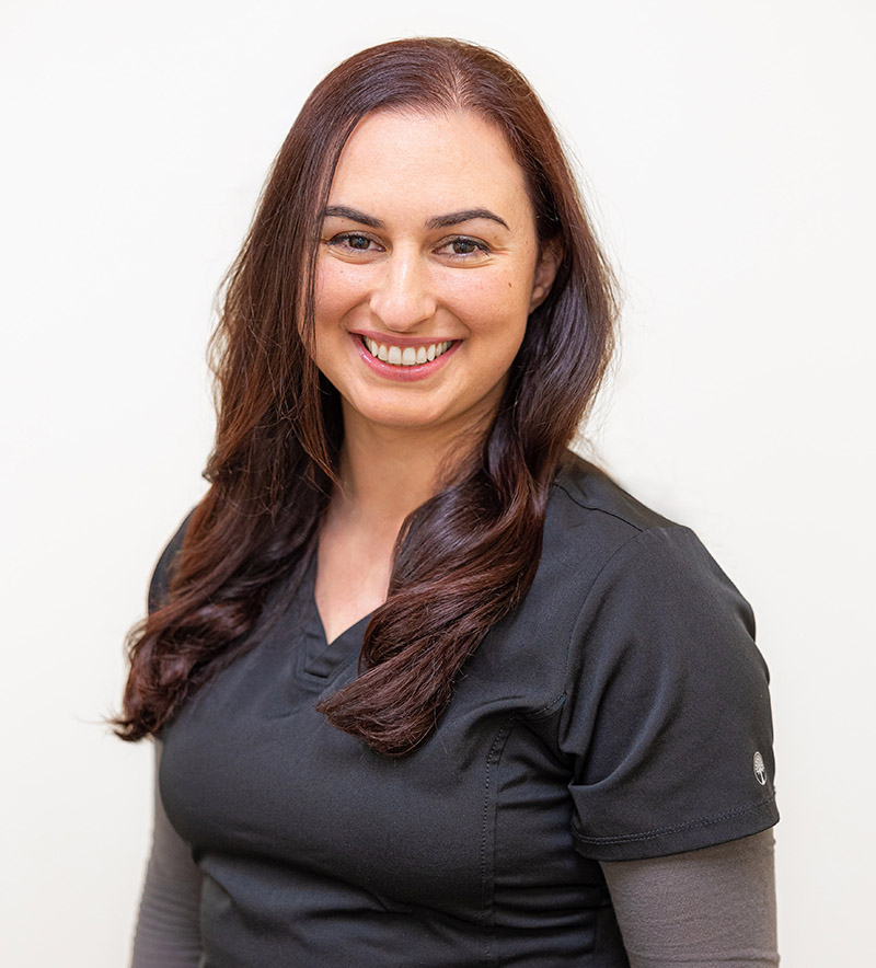 Professional headshot of smiling woman in dark shirt against white background for dental practice.