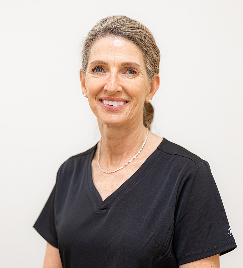 Professional headshot of smiling woman in black scrubs against white background, dentistry office portrait.