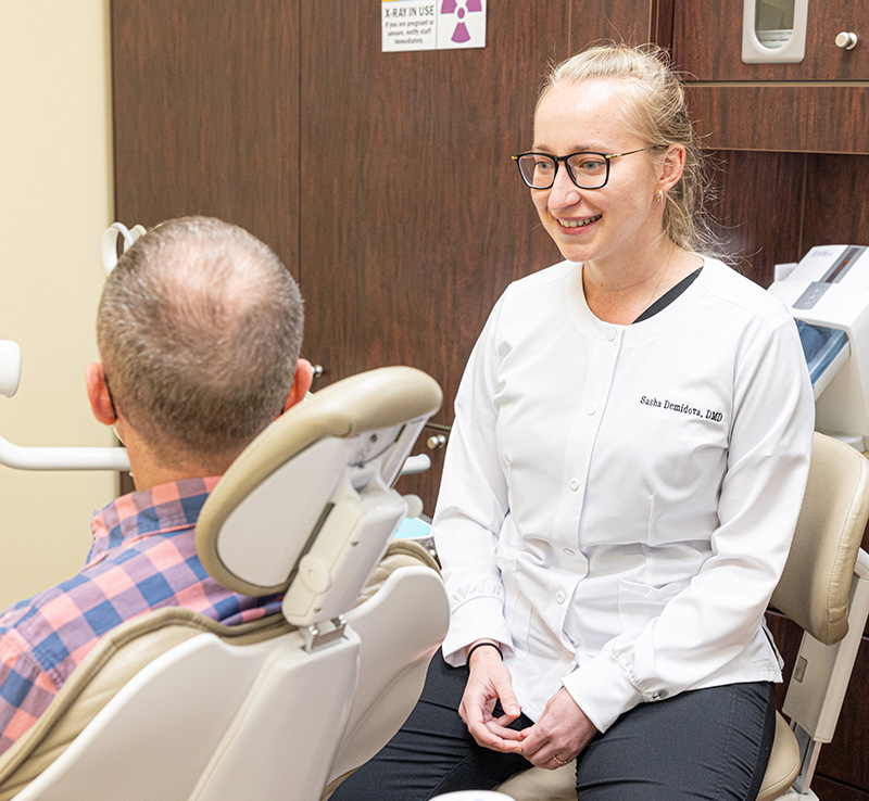 Dentist in white coat smiles while consulting with patient in dental chair at Fletcher Family Dentistry office.