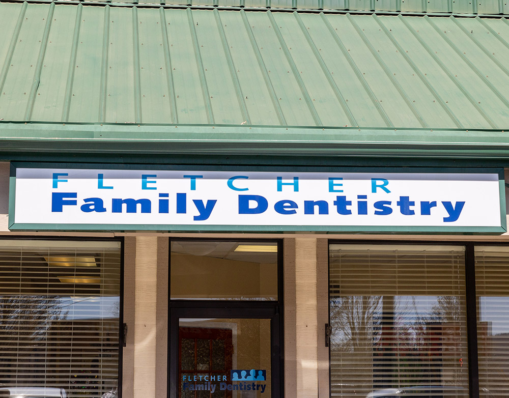 Fletcher Family Dentistry storefront with blue signage and wooden entrance doors on brick building.