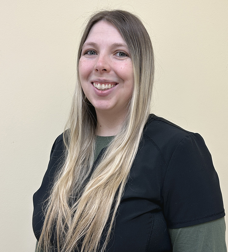 Professional headshot of a smiling woman with long blonde hair wearing a black jacket against a neutral background.