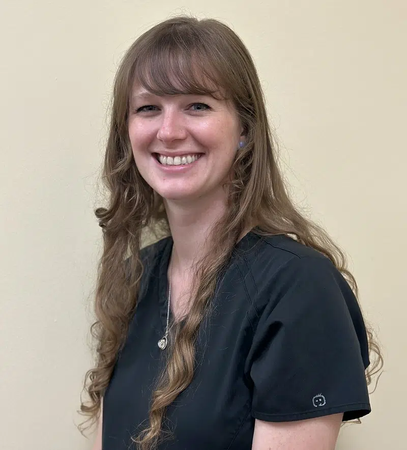 Woman smiling at camera wearing dark scrubs in dental office setting.